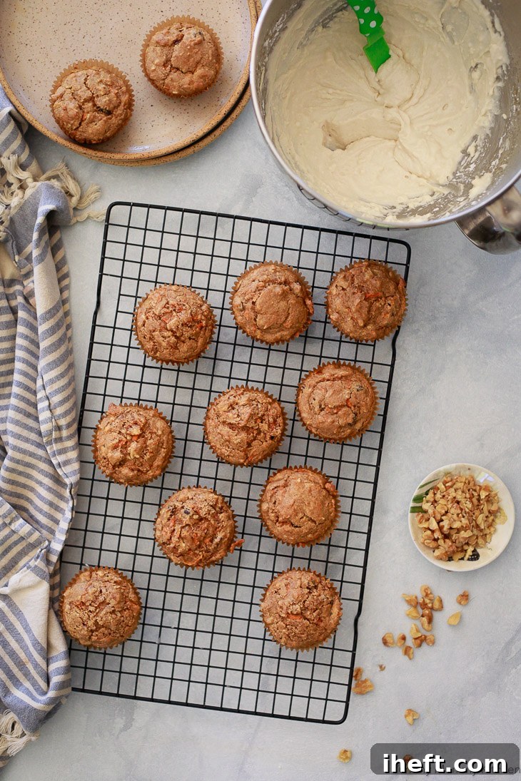 Oat flour gluten-free vegan carrot muffins cooling on a wire rack, awaiting a dollop of creamy vegan cream cheese frosting.