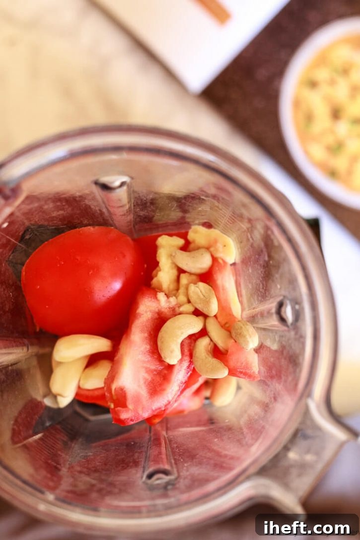 Tomatoes, cashews, ginger, and garlic in a Vitamix blender make a creamy paste for Gobi Matar Instant Pot curry, essential for a rich, plant-based Indian dish.