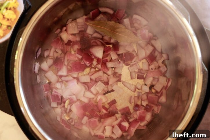 Onions and whole spices like cardamom, peppercorns, and cloves sauté in an Instant Pot for an easy Indian cauliflower and pea coconut curry recipe, filling the kitchen with fragrant aromas.