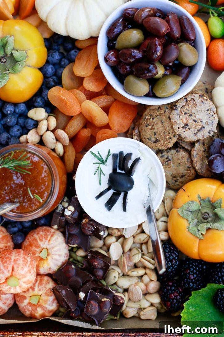 A tantalizing Halloween party platter, perfect for finger food appetizers, showcasing a delightful mix of olives, whimsical olive spiders, charming tangerine pumpkins, assorted fresh fruit, and creamy dairy-free cheese.