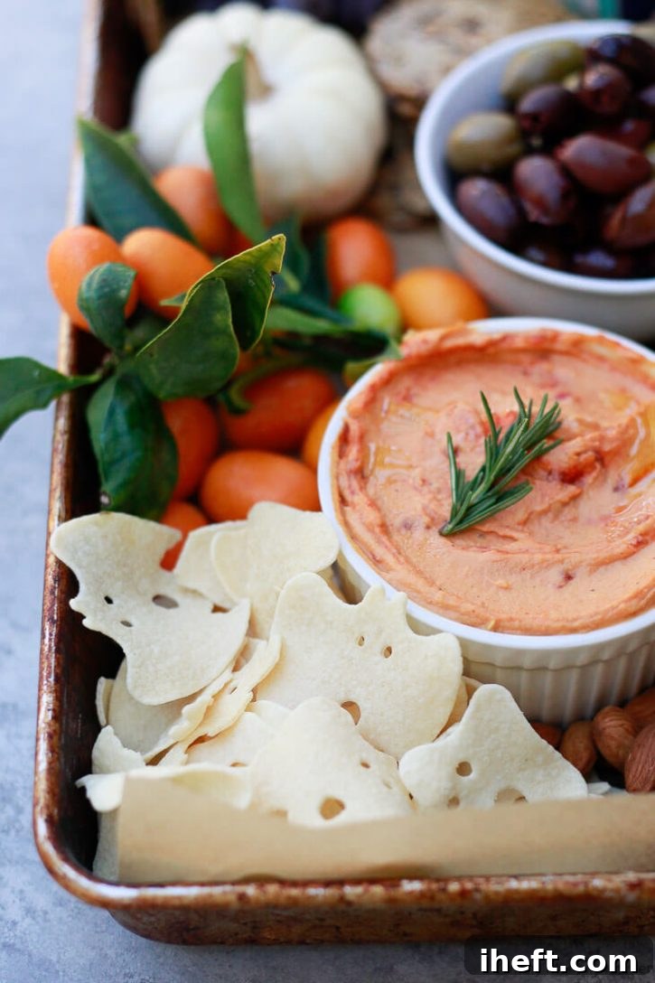 Crunchy Boo chips elegantly presented on a Halloween party platter, surrounded by creamy red pepper hummus, savory olives, fresh fruit, a selection of dairy-free cheese, and various nuts, creating a balanced and festive spread.