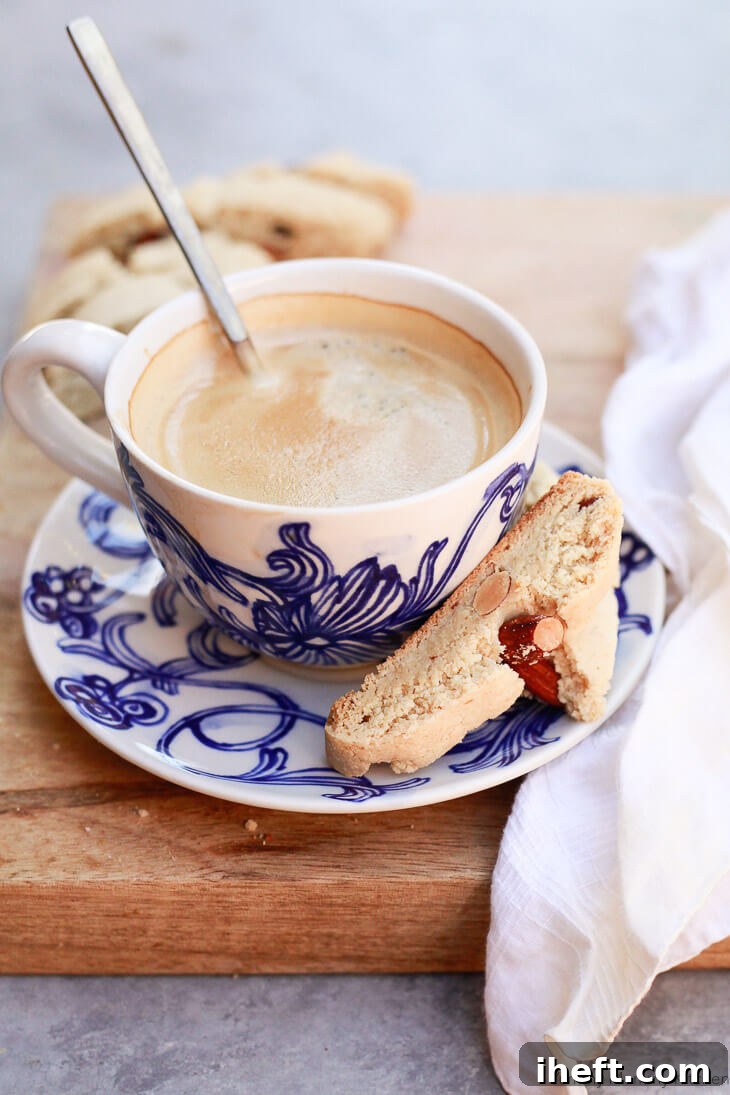 A beautifully composed shot of gluten-free almond cantucci biscotti on a white plate, accompanied by a steaming cup of coffee, inviting indulgence.