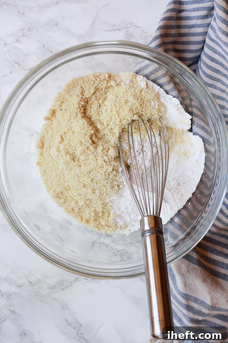 Almond flour and arrowroot starch are being whisked together in a white bowl, representing the initial dry ingredients for gluten-free vegan biscotti.
