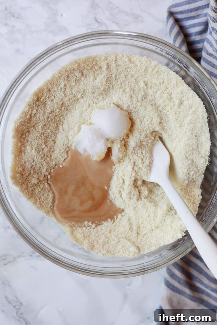 Egg substitute and melted coconut oil are poured into a bowl containing almond flour, illustrating the process of combining wet and dry ingredients for easy gluten-free vegan biscotti.