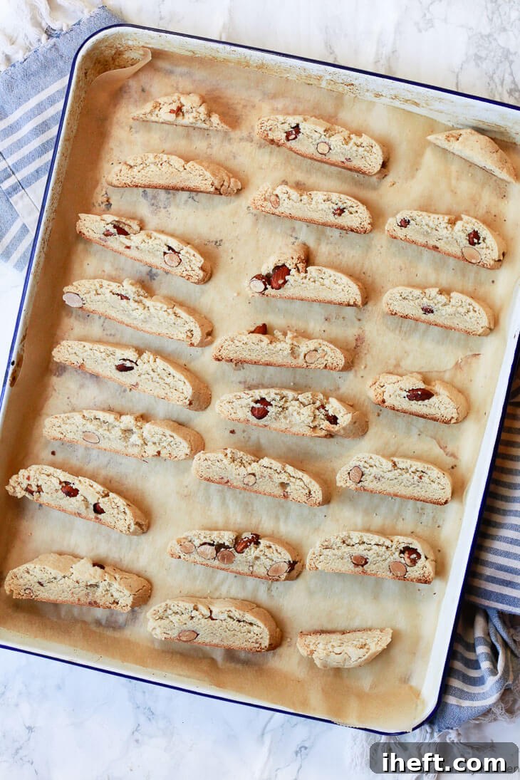 Rows of precisely sliced gluten-free almond biscotti arranged on a cookie sheet, ready for their second baking and final crisping.