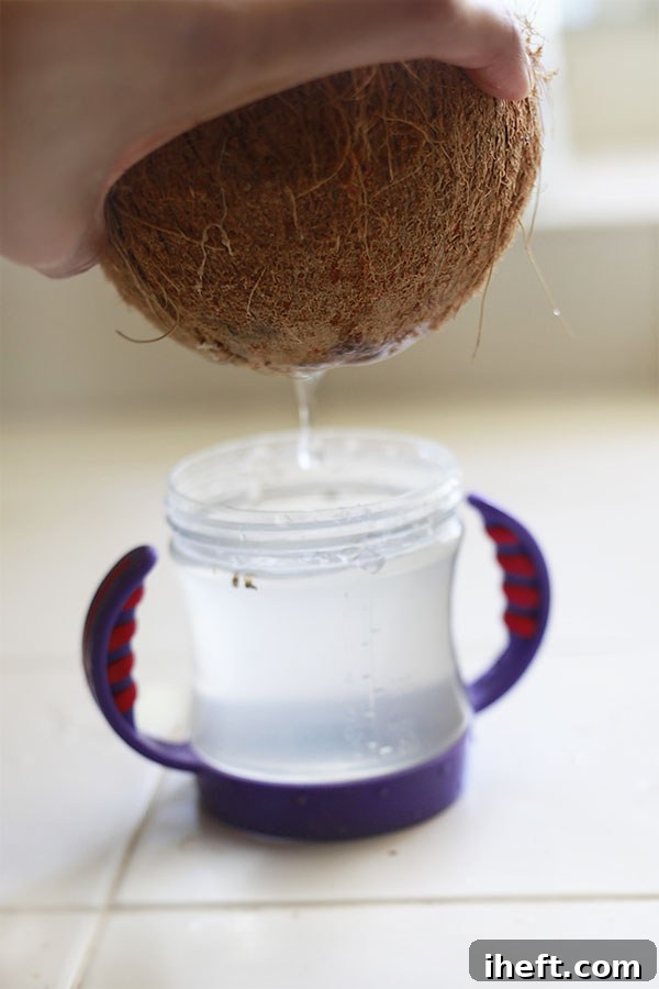 A stream of clear coconut water pouring from a freshly punctured coconut into a glass, highlighting the refreshing liquid.