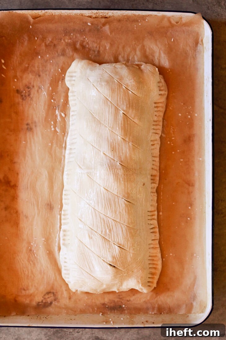 A prepared puff pastry Vegetarian Wellington, generously brushed with coconut milk and elegantly scored with a knife, poised to enter the oven for baking to golden perfection.