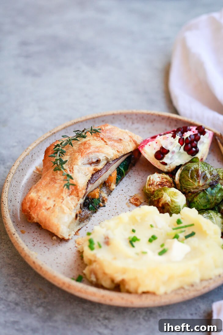 A beautifully plated Vegetarian Wellington for a festive Thanksgiving or Christmas dinner, accompanied by creamy mashed potatoes, crisp Brussels sprouts, and ruby-red pomegranate seeds. This vegan Wellington is generously filled with mushrooms, portobello mushrooms, butternut squash, and spinach, creating a vibrant and satisfying holiday meal.