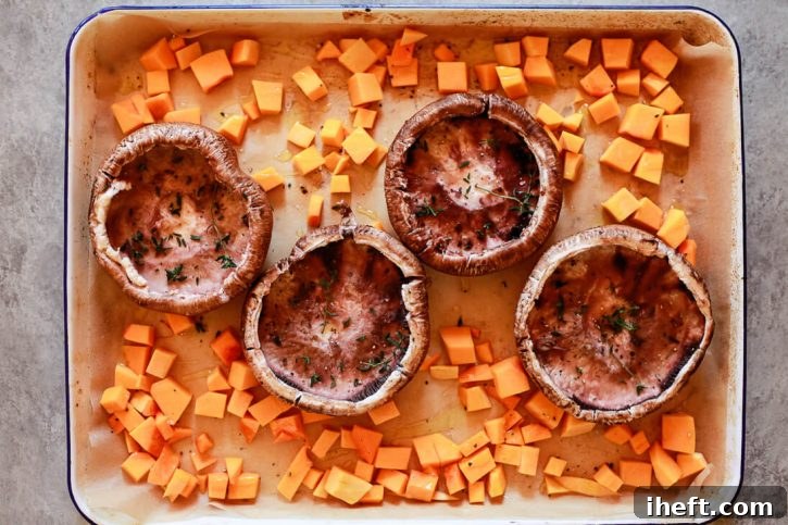 Portobello mushrooms seasoned with fresh thyme and cubes of butternut squash arranged on a sheet pan, ready for roasting to create a flavorful filling for a Vegetarian Wellington recipe.