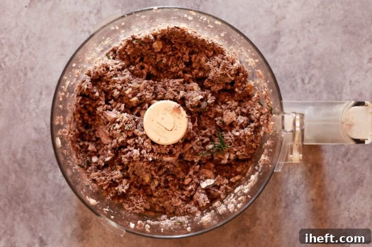 A close-up view of the finely blended mushroom pâté, or duxelles, inside a food processor, showcasing its rich texture and readiness for sautéing.