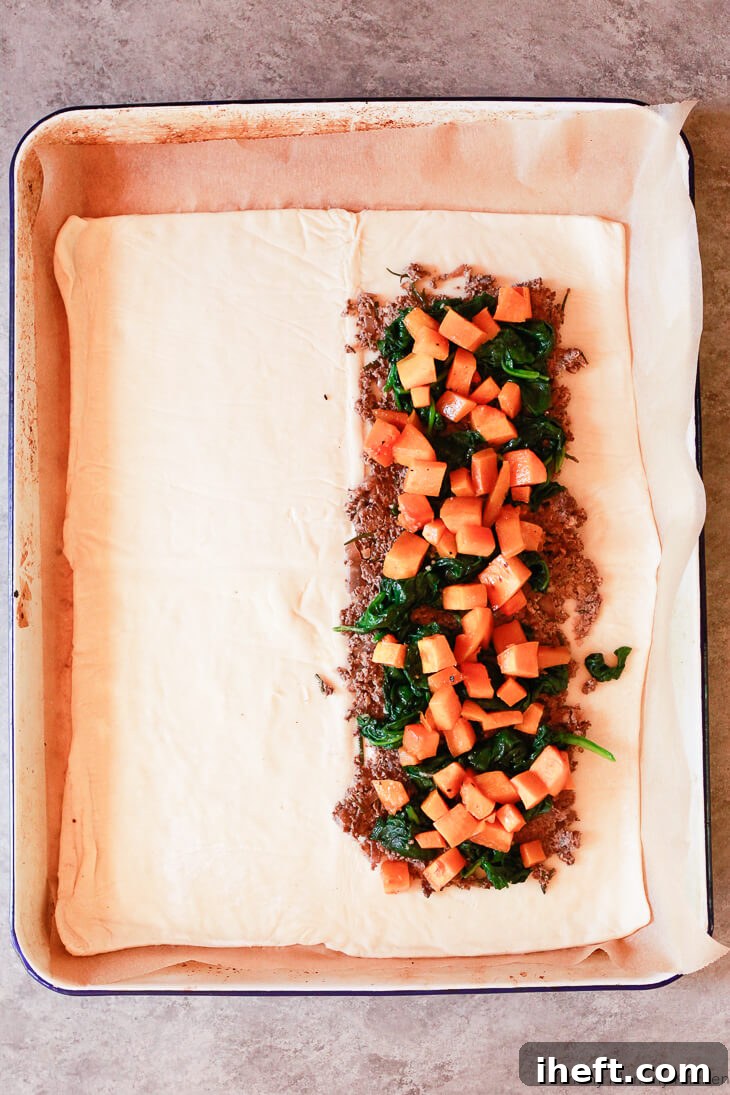 The delicious layers of mushroom duxelles, vibrant spinach, and roasted butternut squash carefully arranged on puff pastry, forming the core of the Mushroom Wellington before the final encasing.