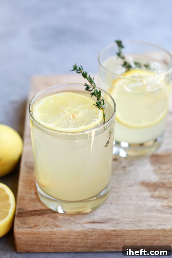 Two glasses of a homemade apple cider vinegar drink with lemon slices sit on a cutting board. 