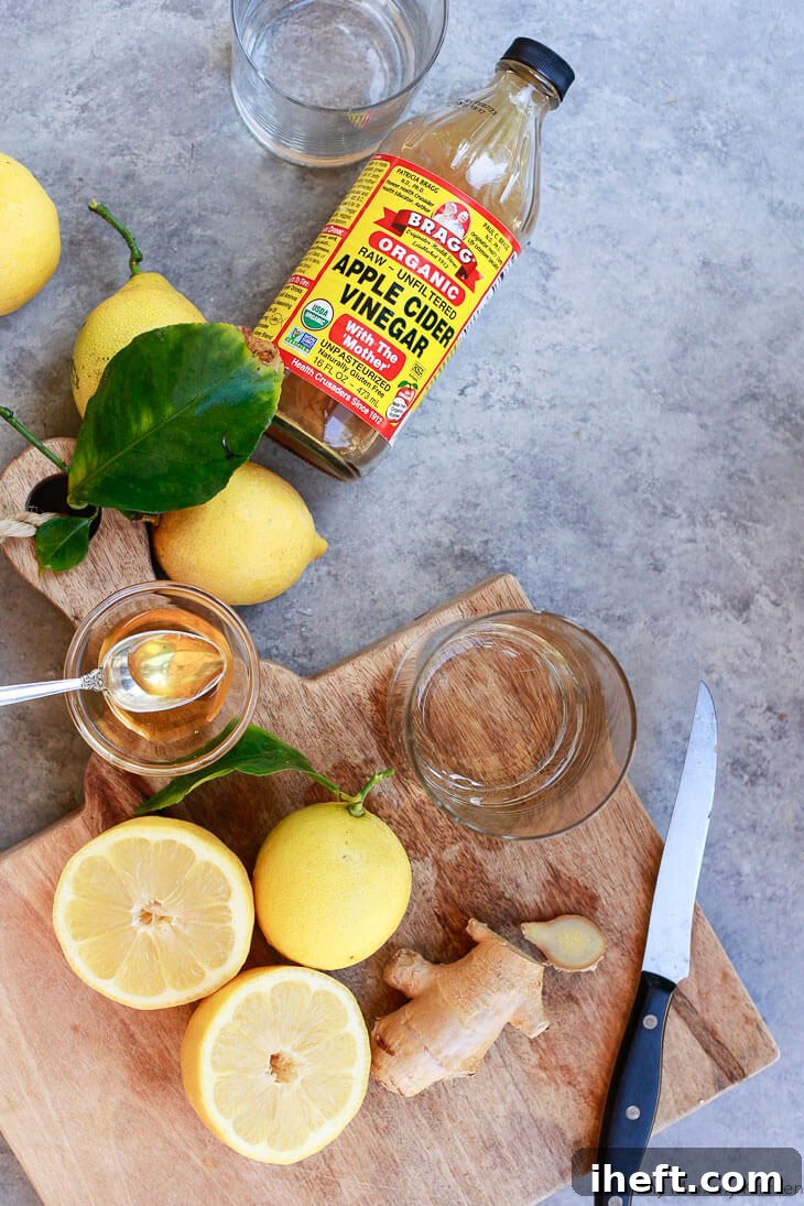 Ingredients for an apple cider vinegar drink recipe including lemons, Bragg ACV, ginger, and honey on a cutting board. 