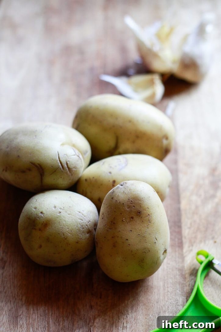 Yukon Gold potatoes on a cutting board with a peeler and garlic. 