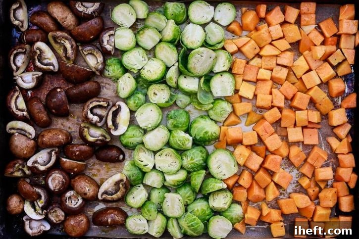 Raw mushrooms, Brussels sprouts, and butternut squash cubes drizzled with olive oil sit on a sheet pan before roasting for vegetable risotto. 