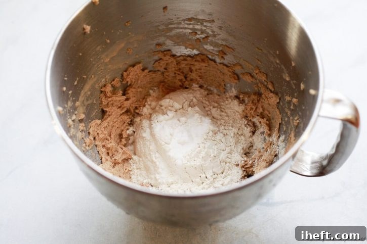 Flour and baking soda are added to the creamed vegan butter, sugar, and egg replacer mixture for vegan chocolate chip cookies, showing the beginning of dough formation.