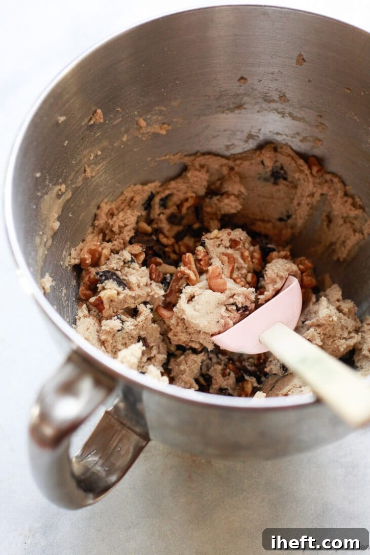 Vegan chocolate chip cookie dough in a mixing bowl, generously studded with chocolate chunks and walnuts, ready for scooping onto a baking sheet.