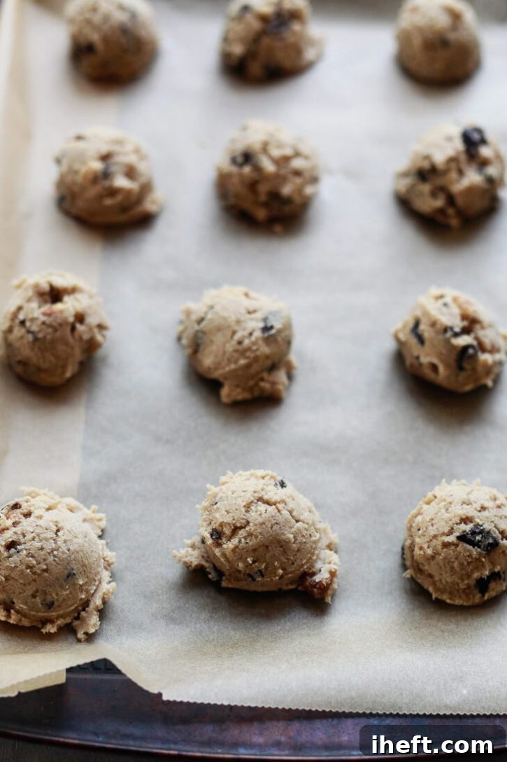 Scoops of vegan chocolate chip cookie dough, perfectly rounded, arranged on a baking sheet lined with parchment paper, awaiting the oven.