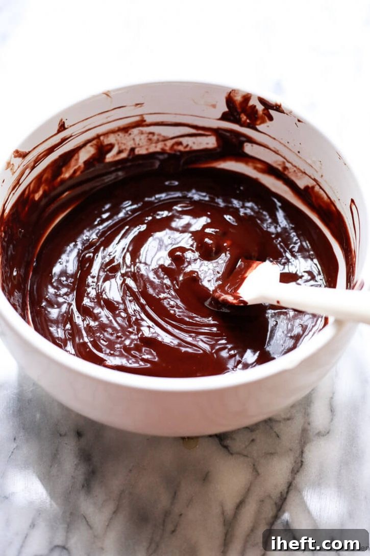 Beautiful shiny melted chocolate and coconut cream ganache in a bowl on a marble counter. 