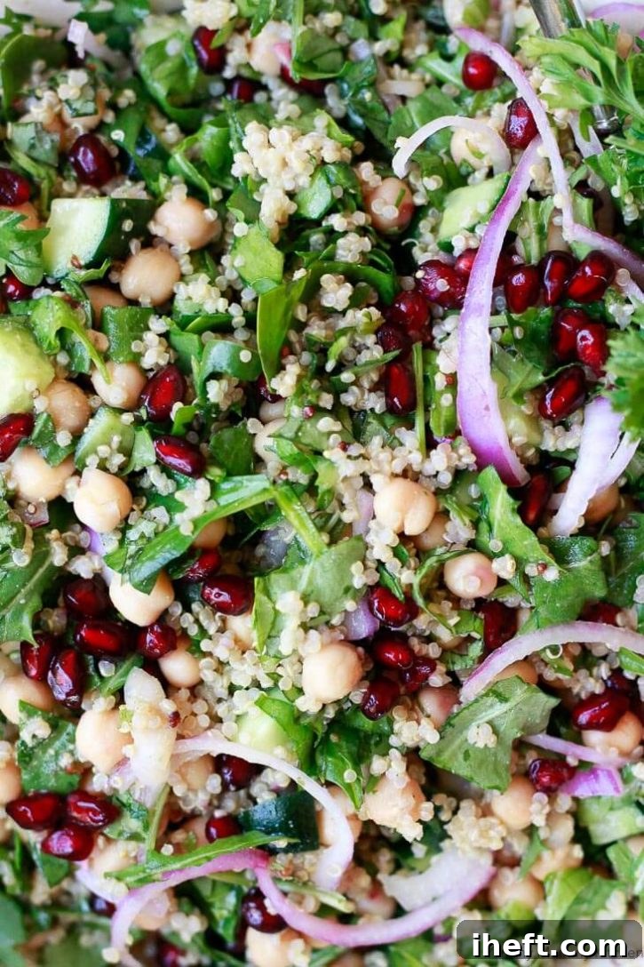 A vibrant close-up of a chickpea quinoa salad, highlighting spinach, red onion, and glistening pomegranate arils. The text suggests adding avocado for the perfect healthy make-ahead meal.
