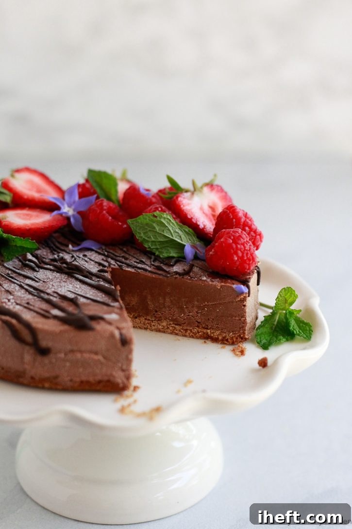 A beautiful vegan chocolate cheesecake topped with berries sits on a cake stand. 