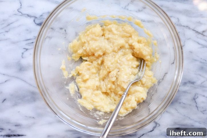 Close-up of ripe, speckled bananas being mashed in a bowl with a fork, ready for banana bread.