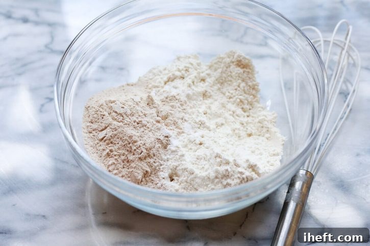 Dry ingredients for vegan banana bread, including flours, baking soda, and salt, sifted into a separate bowl.