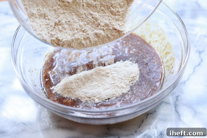 Dry ingredients being gently folded into the wet batter for vegan banana bread with a spatula.