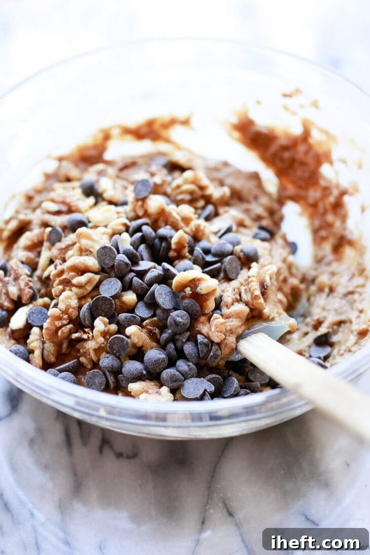 Abundant walnuts and dark chocolate chips being folded into the vegan banana bread batter with a spatula.