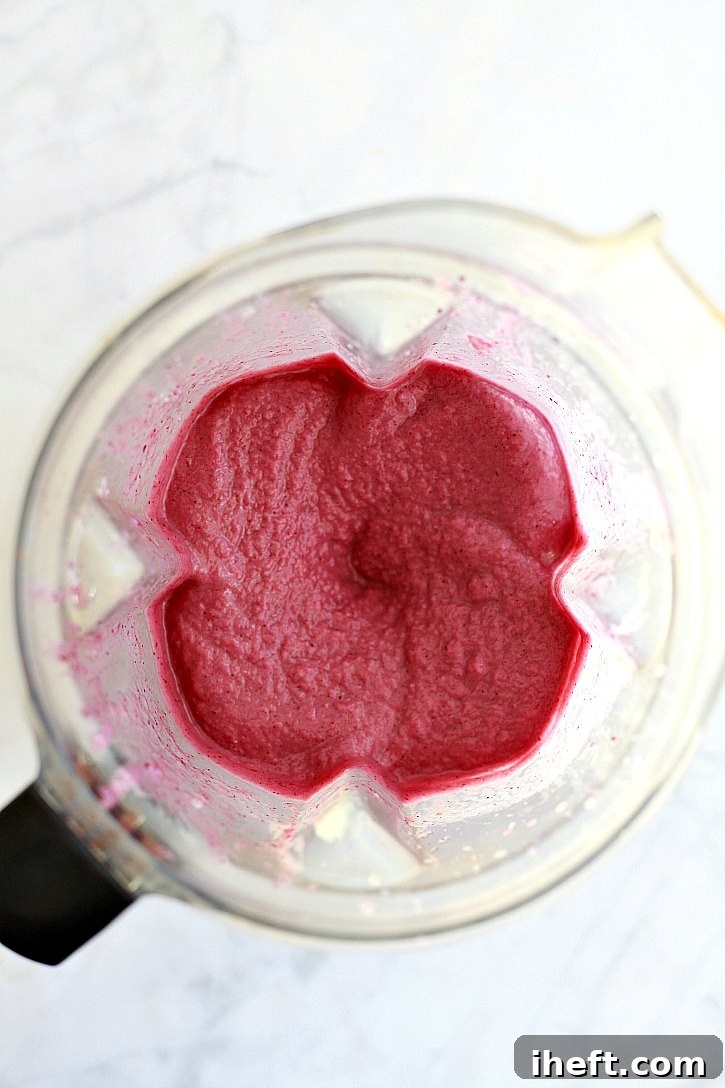 Frozen cauliflower florets being carefully added to a high-speed Vitamix blender, poised to be transformed into a vibrant pink berry smoothie with no detectable vegetable taste.