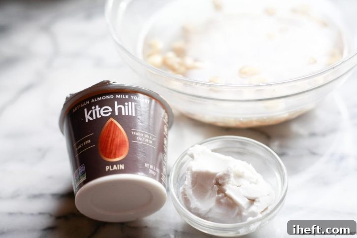The ingredients in this vegan cream cheese recipe sit on a countertop. Plain kite hill yogurt, coconut cream, and soaked cashews. 