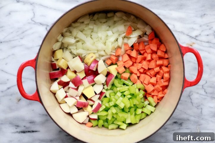 A vibrant mix of chopped onions, carrots, celery, and potatoes glistening in a Dutch oven, signaling the foundational step of a flavorful vegetable soup.