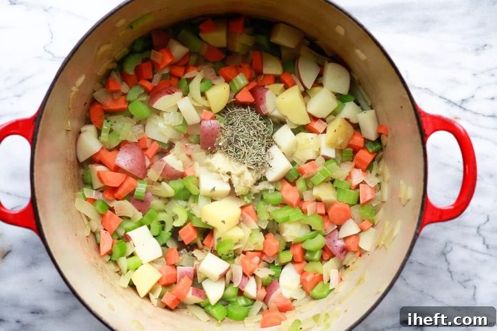 Fresh herbs and minced garlic are carefully placed atop the softening sautéed vegetables in a Dutch oven, poised to infuse a white bean and kale vegetable soup with rich aromatics.