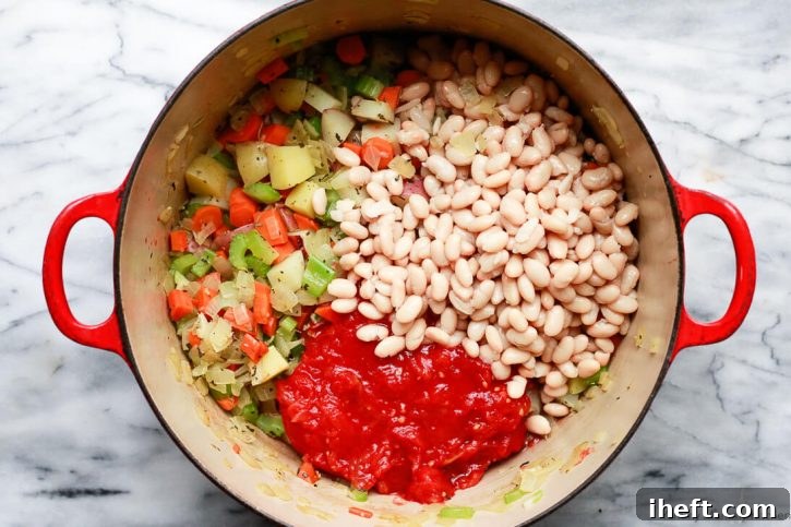Rich crushed tomatoes and creamy cannellini beans are poured into the pot of sautéed vegetables, beginning the simmering process for a delightful white bean and kale soup.