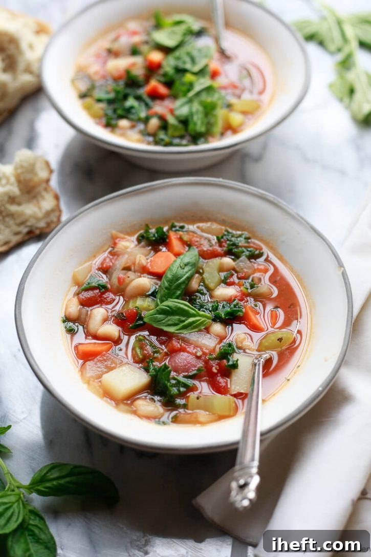 Two white bowls brimming with hot white bean and kale vegetable soup, elegantly garnished with fresh basil leaves and ready to be enjoyed. Spoons are placed in each bowl on a clean marble surface.