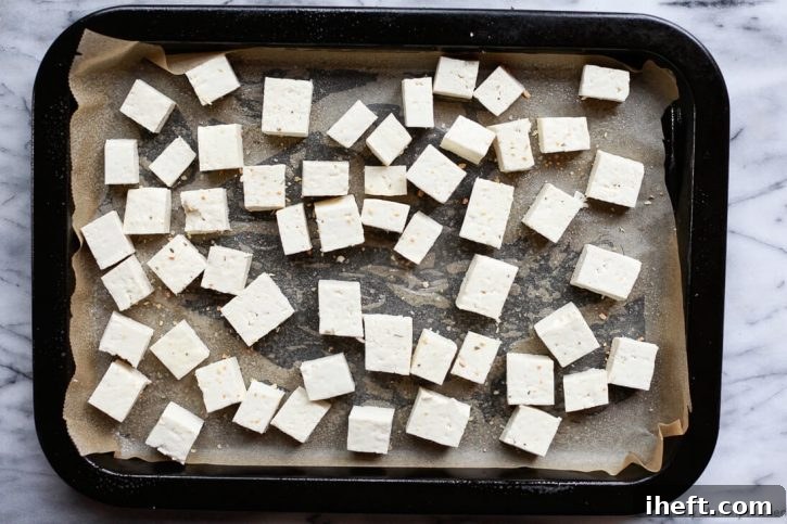 Cubed extra firm tofu meticulously arranged on a parchment-lined baking sheet, seasoned and ready for the oven to achieve optimal crispness.