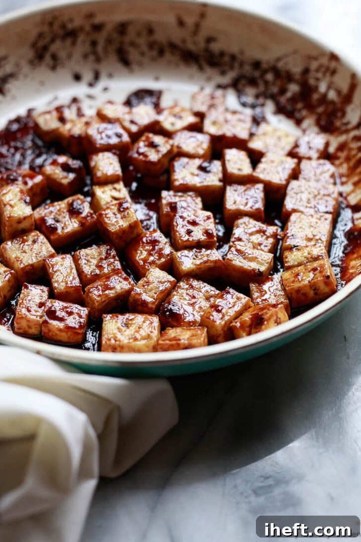 A frying pan filled with perfectly baked tofu, now glistening and thoroughly coated in a rich, sticky, sweet, and savory soy sauce ginger glaze.