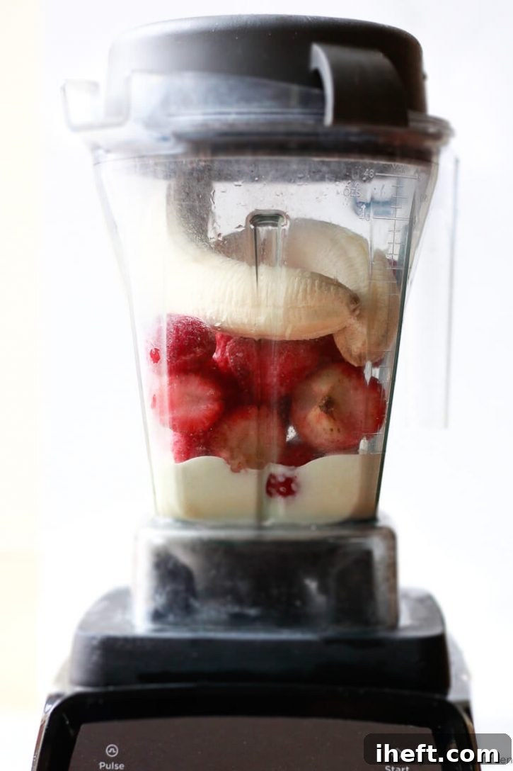A vitamix blender filled with yogurt, frozen strawberries, and fresh bananas. 
