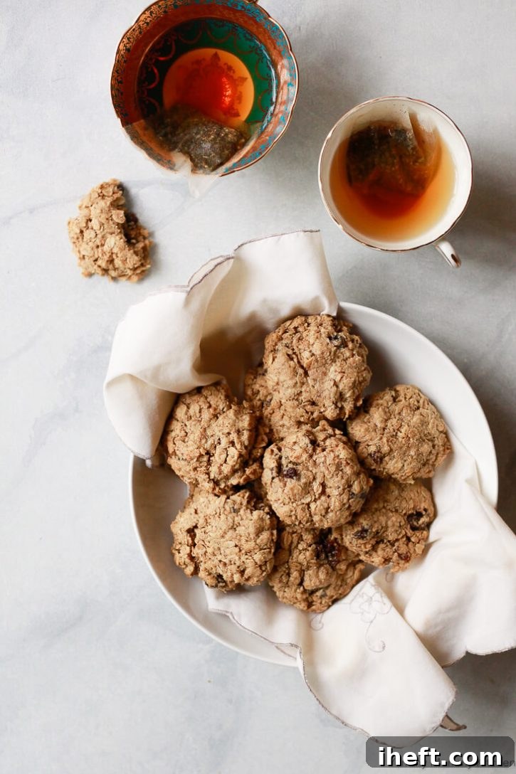 A white bowl filled with classic chewy oatmeal raisin cookies on a marble counter with two cups of tea. 