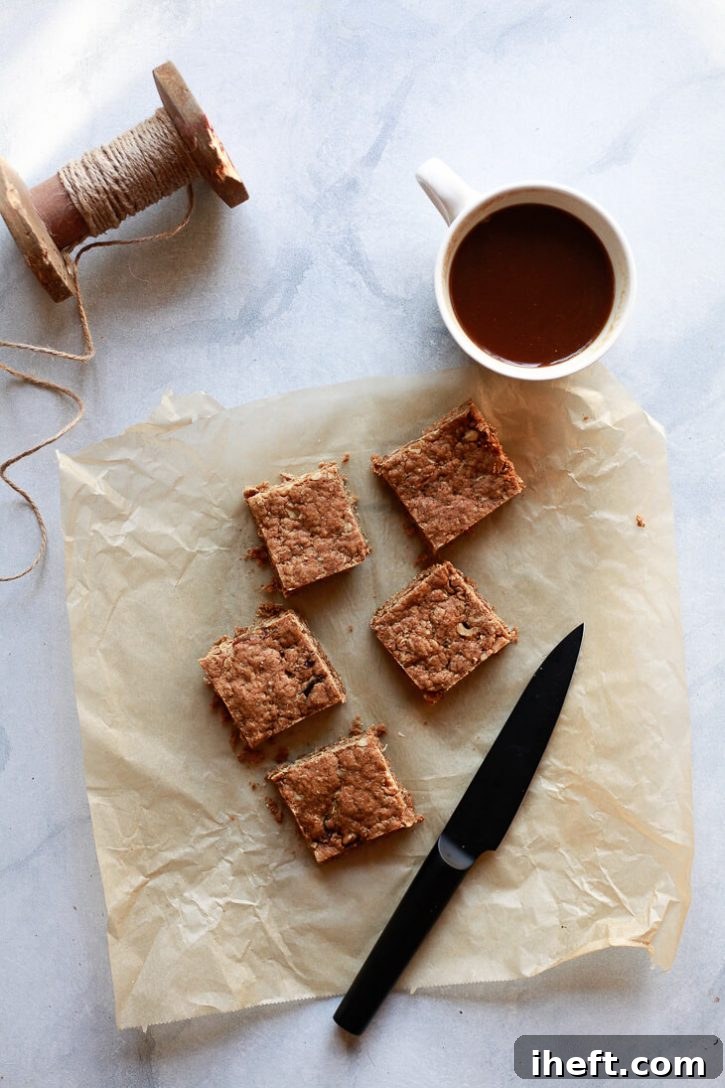 Freshly baked peanut butter oatmeal snack squares, perfectly cut and arranged on parchment paper, showcasing their delicious golden-brown crust. These high-protein vegan bars offer a delightful combination of granola bars, blondies, and snack cake, ideal for a portable and energizing treat.