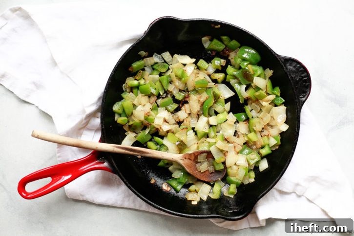 Onions and green bell pepper saute in a red cast iron skillet to start making vegan sloppy joes. 