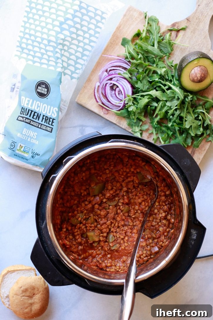 Vegan lentil sloppy joes in an Instant Pot pressure cooker with toppings on a cutting board including avocado, arugula, and red onion. 