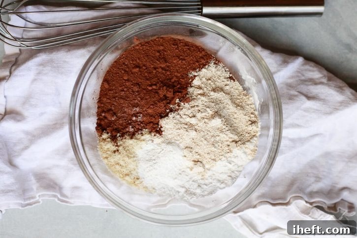 The dry ingredients for chocolate banana muffins in a glass bowl include cocoa powder, almond flour, oat flour, and tapioca flour.