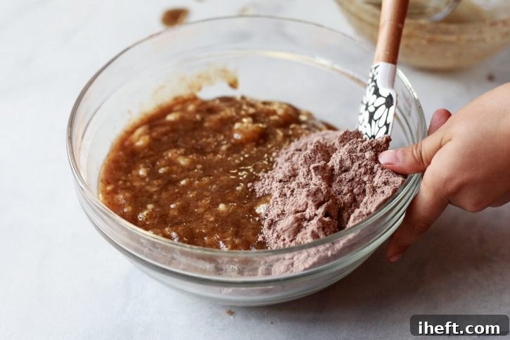 The wet and dry ingredients for chocolate banana muffins get folded together in a glass bowl.