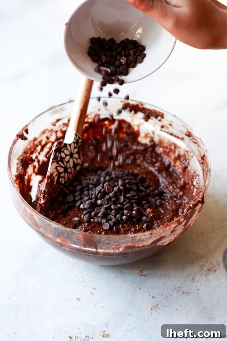 A small bowl of mini chocolate chips gets poured into chocolate banana muffin batter.