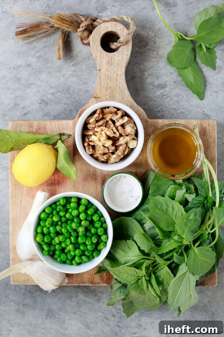 Ingredients for vegan pea and basil pesto on a wooden cutting board: whole lemon, bowl of walnuts, bowl of peas, fresh basil, garlic, salt, and olive oil. 