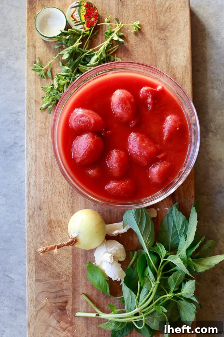 The essential ingredients for a classic pomodoro sauce laid out on a wooden cutting board: a bowl of vibrant whole peeled San Marzano tomatoes, fragrant fresh basil leaves, a neatly diced yellow onion, peeled garlic cloves, fresh oregano sprigs, and a sprinkle of sea salt.