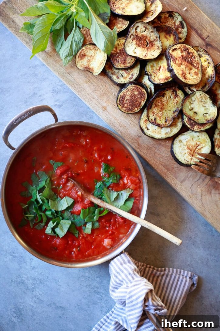 A large pan brimming with freshly made homemade pomodoro sauce and fragrant basil, resting on a sleek grey surface. Next to it, a wooden cutting board holds a stack of beautifully cooked eggplant rounds, suggesting a delicious pairing.