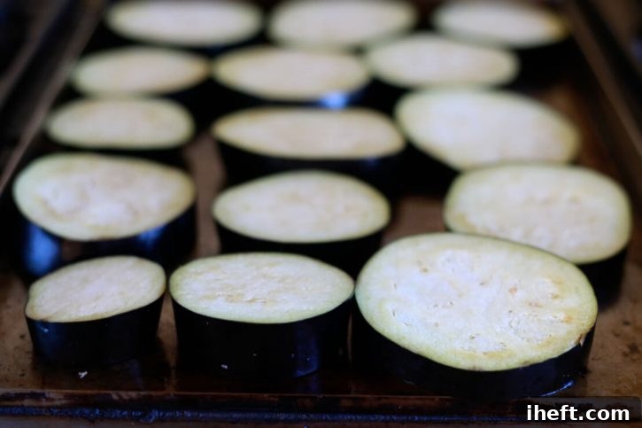 Sliced eggplant rounds begin to cook on a griddle to make healthy vegan eggplant parmesan. 