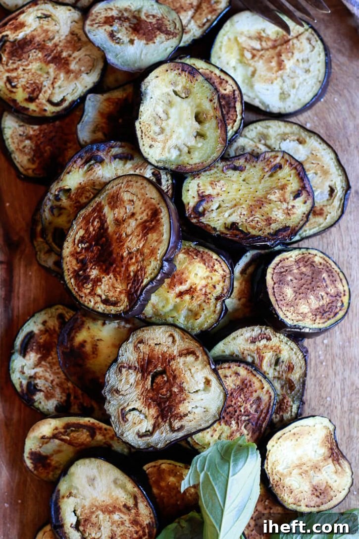 Beautiful browned eggplant slices sit on a cutting board ready to be assembled into a healthy vegan baked eggplant parmesan. 